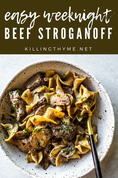 a white bowl filled with beef stroganoni next to a black spoon and fork