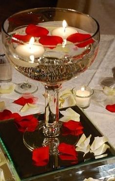 candles are lit in a glass bowl on a table with rose petals and petals around it