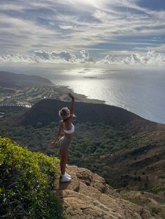 a woman standing on top of a cliff with her arms in the air and looking at the ocean