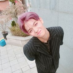 a young man with pink hair is taking a selfie in front of a building