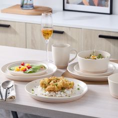 a table topped with white plates and bowls filled with food next to glasses of wine