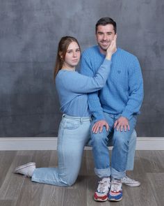 a man and woman sitting on the floor with their hands behind their heads, posing for a photo