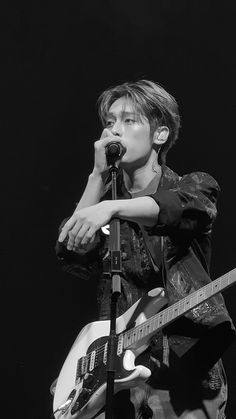 a young man holding a guitar while standing next to a microphone in front of him