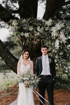 a bride and groom standing in front of a large tree with white flowers on it