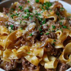 a white bowl filled with pasta and meat covered in gravy, garnished with parsley