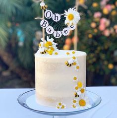 a white cake with daisies on top and one bake spelled out in letters