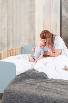 a woman holding a baby in her arms while sitting on a bed with a wooden headboard