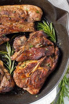 some meat is cooking in a skillet on the stove with rosemary sprigs