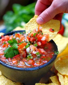 a hand dipping a tortilla chip into a black bowl filled with salsa and garnished with cilantro