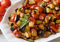 a white plate topped with cooked vegetables next to tomatoes