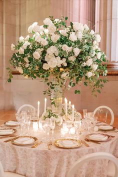 the centerpiece is surrounded by white flowers and greenery, along with gold chargers