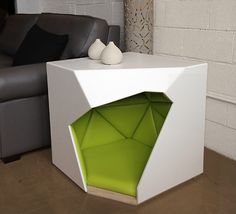 a white table with an open green box on it's side in front of a couch