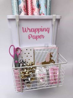 wrapping paper in a basket with scissors and other crafting supplies next to the sign