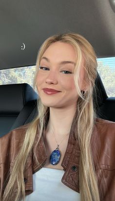 a woman sitting in the back seat of a car with long blonde hair and wearing a brown leather jacket