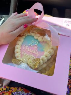 a person holding a pink ribbon over a cake in a box with the number 23 on it