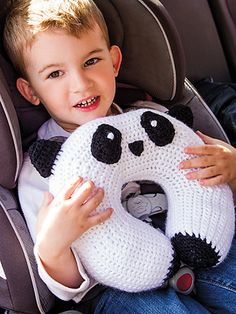 a young boy in a car seat holding a panda bear stuffed animal with black and white crochet