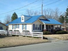 a small white house with blue roof next to a street