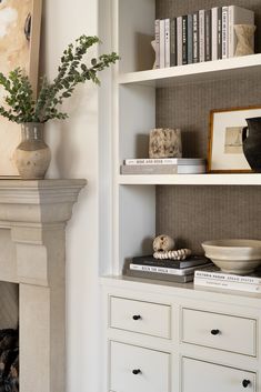 a white book shelf with books on it and a vase filled with flowers in the corner