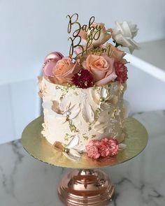 a white and gold cake with pink flowers on the top is sitting on a table