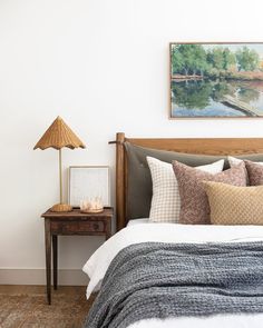 a bed with pillows and blankets on top of it next to a night stand in front of a painting