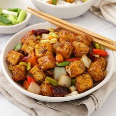 a bowl filled with tofu and vegetables next to chopsticks on a table