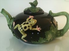 a frog sitting on top of a black tea pot