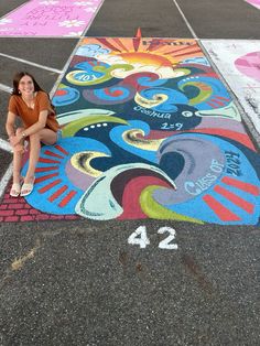 a woman sitting on the ground in front of a parking lot painted with colorful designs