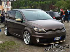 a brown car parked on top of a dirt road next to other cars and people