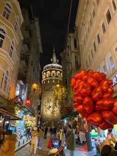 people are walking down the street at night with red balloons in the foreground and an ornate building on the other side