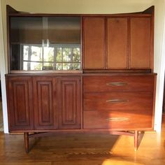 a large wooden cabinet sitting on top of a hard wood floor next to a window