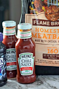 three bottles of hot sauce sitting on top of a counter next to a bag of meat