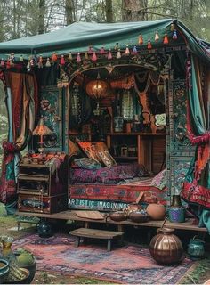 an old bed is covered with colorful fabric and tassels in the middle of a forest