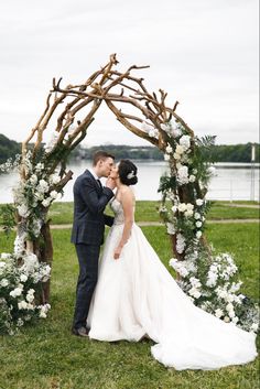 a bride and groom kissing in front of an arch made out of branches with white flowers