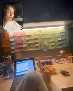 a woman sitting in front of a laptop computer with sticky notes on the wall behind her