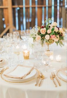 the table is set with white linens and gold place settings