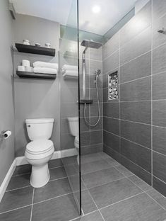 an image of a bathroom with gray tile and white fixtures on the walls, along with a glass shower door