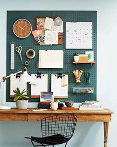 a wooden desk topped with lots of clutter next to a wall mounted bulletin board