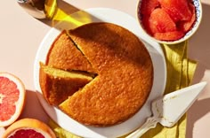 a cake with slices cut out on a plate next to sliced grapefruits