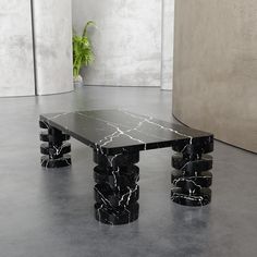 a table with black marble on it in front of a wall and potted plant