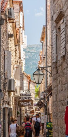 people are walking down an alley way with stone buildings and shutters on either side