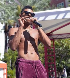 a man with no shirt on is holding a microphone to his mouth and wearing sunglasses