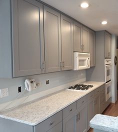 a kitchen with gray cabinets and marble counter tops, white appliances and wood flooring