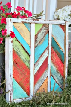 an old wooden box is decorated with colorful wood planks and flowers in the background