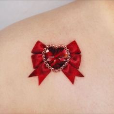 a woman's back with a red bow and heart tattoo on her left shoulder