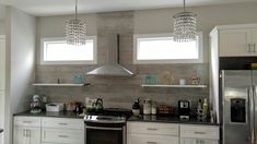 a modern kitchen with stainless steel appliances and white cabinetry, along with two chandeliers hanging from the ceiling