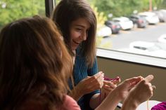 two women are sitting at a table and one is knitting the other's yarn