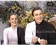 a man and woman sitting next to each other in front of a wall with flowers