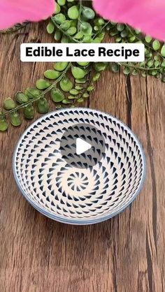 a white and blue bowl sitting on top of a wooden table next to green plants