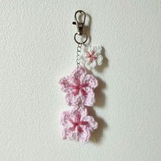 a crocheted flower key chain hanging from a hook on a white wall background