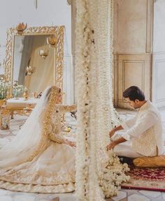 a bride and groom sitting on the floor in front of a mirror with pearls all over it